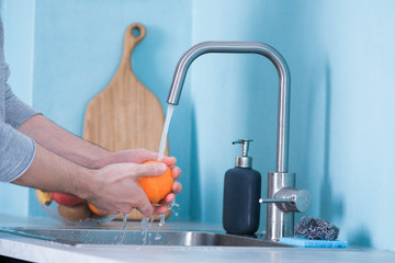 A man washes fruit in a sink in a kitchen with blue walls. Against the background of fruits. Men's...