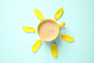 Cup of morning coffee and tulip petals on light blue background, flat lay
