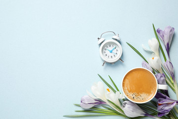Fototapeta na wymiar Cup of morning coffee, crocuses and alarm clock on light background, flat lay. Space for text