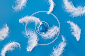 Easter background with a blue colored egg and a white bird's feather