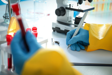 Fototapeta premium Scientist in chemical protective suit working with blood samples at table, closeup. Virus research