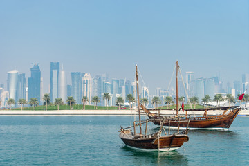 Fototapeta premium Retro historical boat with blurred panoramic view of modern skyline of Doha and green palms on background