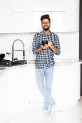 Handsome indian bearded man on kitchen is smiling and drinking coffee in the morning.