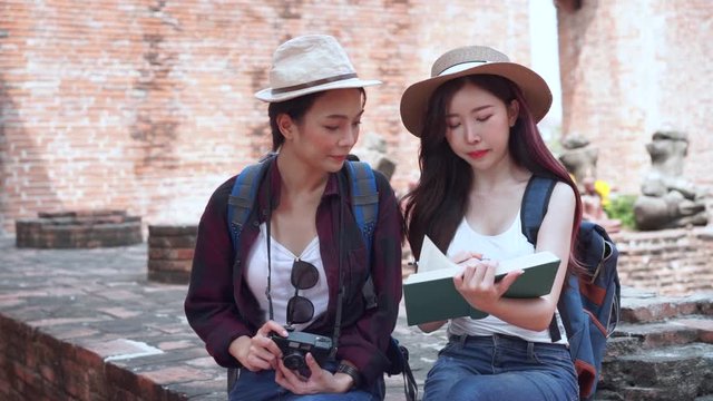 Two Archeology students on a field trip take a photo and record to notebook together at Ayutthaya Historical Park, Thailand.