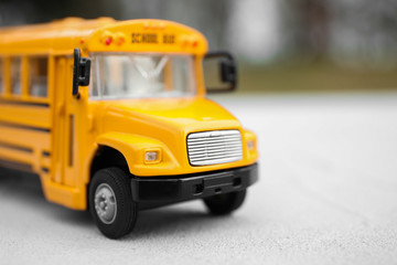 Yellow toy school bus against blurred background, closeup. Transport for students
