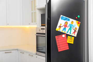 Modern refrigerator with child's drawing, notes and magnets in kitchen. Space for text