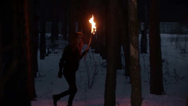 Young lost woman with torch walking in the night forest