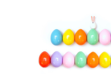 Top view of an Easter composition of painted eggs in bright juicy colors on a white background with a little rabbit. Holiday concept, flat layout, minimalism