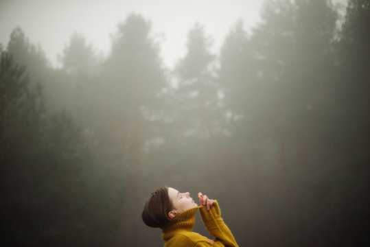 Thoughtful woman standing by forest in foggy weather