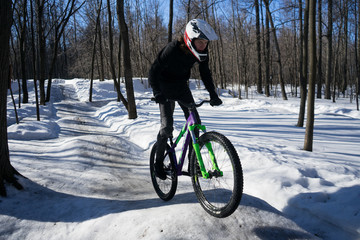 A cyclist in a helmet rides on a pump track in winter. Mtb rider rides a bike on a snowy track