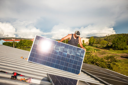 worker instals solar panels on top of building.