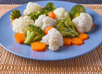 Vegetables on a grey plate over a wood mat. Broccoli, cauliflower and carrot cooked. Healthy vegan food.