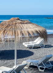 Thatched parasols on black voulcatic lava sand beach