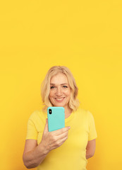 Pretty adult lady in bright clothes watching camera and posing with blue phone