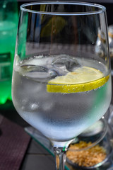 Drinking cold mineral water with bubbles, served in wine glass with ice cubes and lemon