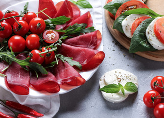 The concept of Italian cuisine. Italian dried ham from beef. Meat snack. Bresaola with arugula and tomatoes, mozzarella, basil and chili pepper. Caprese. Background image, copy space
