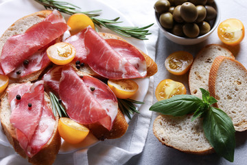 The concept of Italian cuisine. Coppa - Italian dried sausage made from pork neck. Meat snacks. Baguette, olives, cherry tomatoes, rosemary, basil on a light white background.  copy space