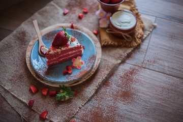 Red Velvet cake on a blue plate with strawberries, pure cocoa and cream cheese with a rustic background with flowers and cloth napkins