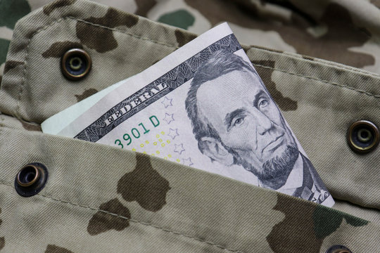 The bollar note lies in a pocket of a camouflage uniform.