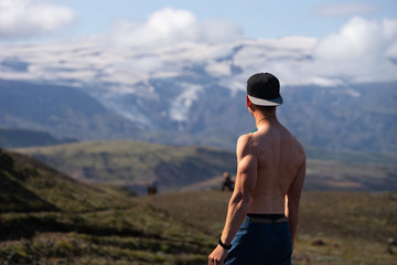 Backside of tall muscular caucasian man with naked torso standing in over mountain and sky background. Promoting active, sport and healthy lifestyle