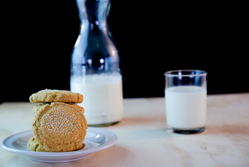 amaranth cookies floating in the air with black background and in the background a cup of milk