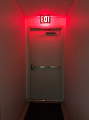 Emergency exit door at the end of the hall with the exit light on. - obrazy, fototapety, plakaty