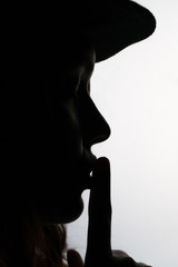Silhouette portrait of young female model showing silence gesture. Black and white noir style