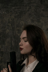 Vertical portrait of young brunette female model blowing on gun barrel. Female agent concept. - obrazy, fototapety, plakaty