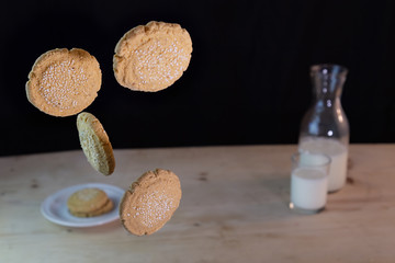 amaranth cookies floating in the air with black background and in the background a cup of milk