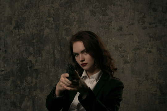 Noir style vertical portrait of young female brunette model pointing a gun towards camera.