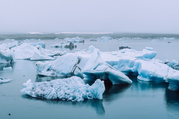 Fototapeta na wymiar Glaciers covered with dense fog in the blue waters of Jokulsalron glacial lake in Iceland