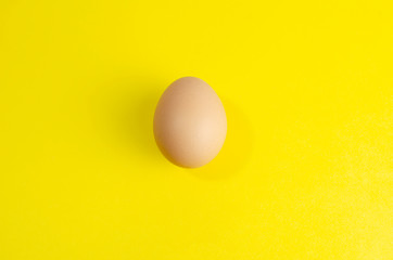 one fresh brown chicken egg on a yellow background