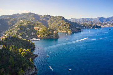 Fototapeta na wymiar Yachts and boats are sailing in the Ligurian Sea on the mountain background, Portofino, Italy. Rocks and hills seaside with the traditional Italian houses on the top.