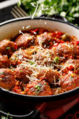 Meatballs in tomato sauce with the addition of aromatic herbs sprinkled with cheese in an enamel rustic dish, close up