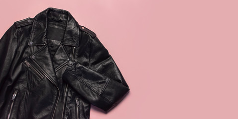 Black women's leather jacket on pink background top view. Fashionable modern trendy women's clothing. Vintage biker jacket. Black genuine leather