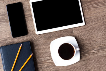 Smartphone and tablet with black screens on a wooden background with cup of black coffee. Blue-black planner and two pencils on it lie next to them.