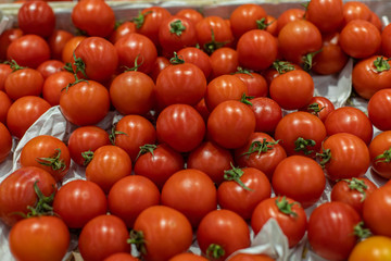 Small red cherry tomatoes with a leaf, top view. Pile of ripe red tomatoes in a crate in a supermarket. Fresh Vegetables Department