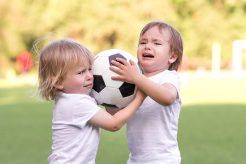 Two little toddlers arguing at football field or playground over soccer ball trying to take or grab ball. Conflict management, corporate fight metaphor and conflict resolving concept - obrazy, fototapety, plakaty