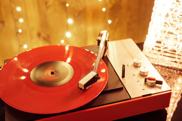 Red vinyl record on turntable, stylus needle and listens to music against of glowing Christmas...