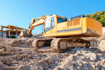 Large yellow construction equipment is digging pit for the base of residential complex with an industrial jackhammer. Construction of large residential building. Initial construction phase