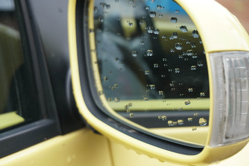 Drops of rain soaked in the rearview mirror of a yellow car