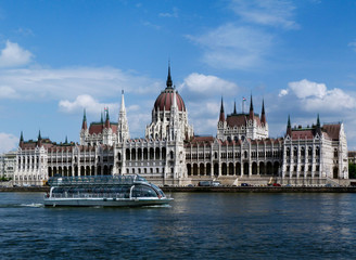 Fototapeta premium the Hungarian Parliament in Neo-Gothic style seen from across the Danube. Famous and popular landmark and tourist attraction in Budapest. panoramic view. white tour boat. City skyline. blue sky.