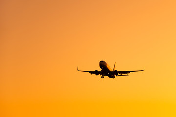 Fototapeta premium Large airliner passengers view is landing on the landing strip at the airport against the backdrop of bright orange sunset on a sunny summer day. A plane flies in the sky at sunset day