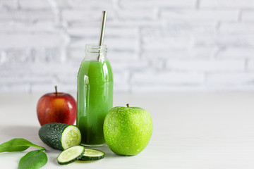 Bottle of detox green smoothie made with green and red apple, spinach and cucumber on white wooden table.
