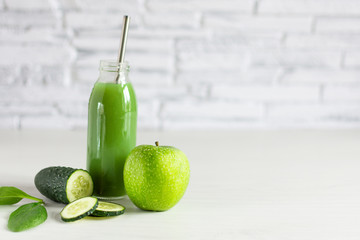 Bottle of detox green smoothie made with apple, spinach and cucumber on white wooden table.