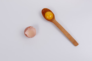 Egg yolk in a wooden spoon, next to the eggshell