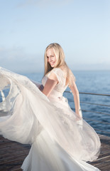 Fototapeta na wymiar happy bride in a wedding dress,wedding outfit bride,young duffel is spinning in a wedding dress on a background of the sea,morning wedding photo shoot of the bride,bride portrait