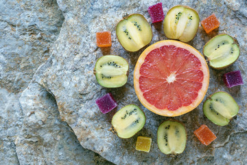 Fruits and fruit jelly candy. Half of grapefruit, halves of kiwi  and slices of marmalade look like flower.. Natural stone background. Flat lay, free space for text