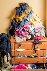open chest drawers with drop-down clothes and piles of clothes around in a mess