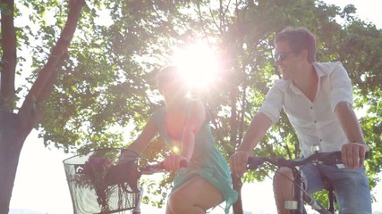SLOW MOTION, CLOSE UP: Happy Caucasian woman and her handsome boyfriend smile while riding their bicycles down a idyllic avenue. Young tourist couple explores the scenic park in Ljubljana by bike. - Powered by Adobe